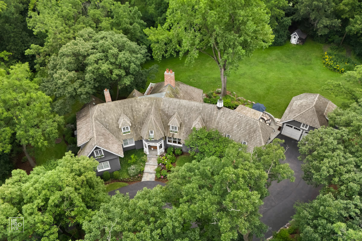 Aerial view of a large shingled home set among dense mature trees with a circular drive — drone photography