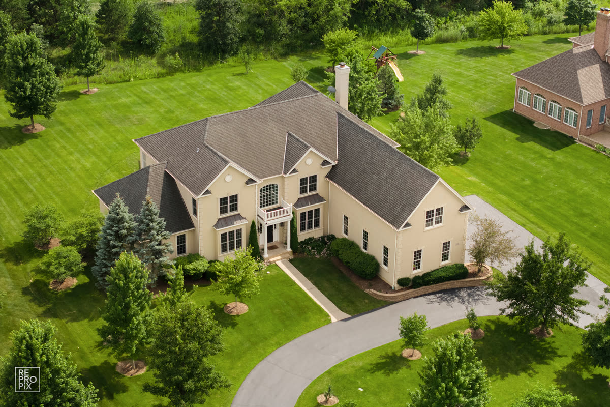 Aerial view of a tan two-story home with steep gables on a wide green lawn — real estate drone photo