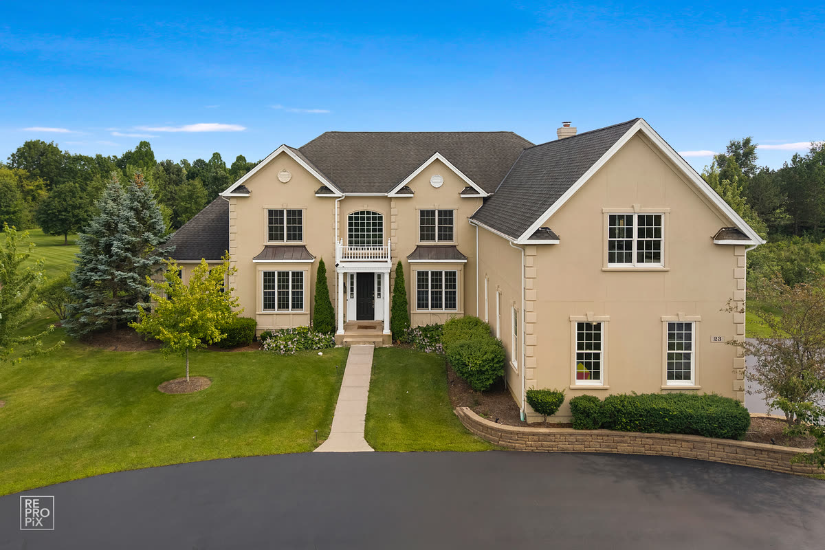 Aerial view of a tan colonial home with an arched entry and a long driveway under a deep blue sky — drone photography