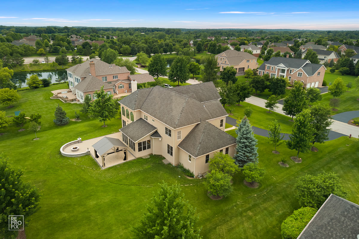 Aerial view of a gabled tan home in an open subdivision with a distant treeline — drone photography