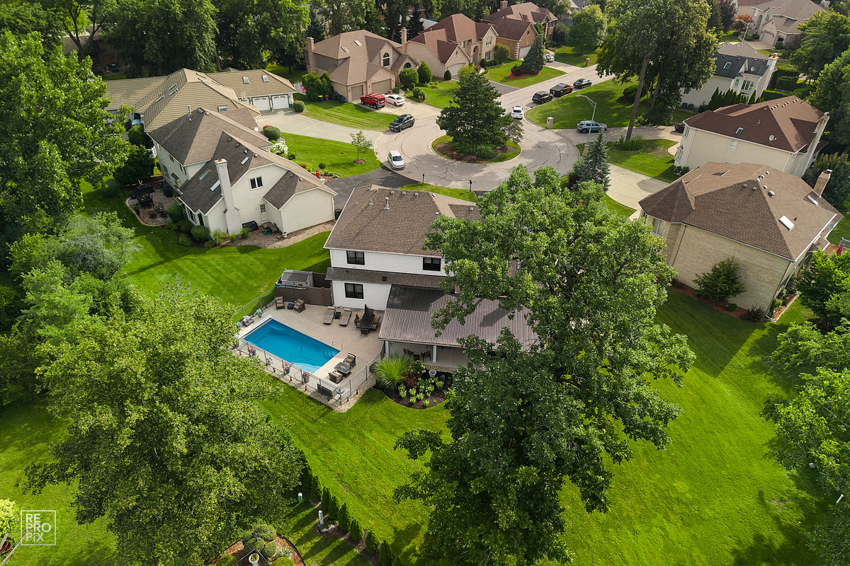 Aerial view of a home with a swimming pool and patio surrounded by mature trees — backyard drone photo