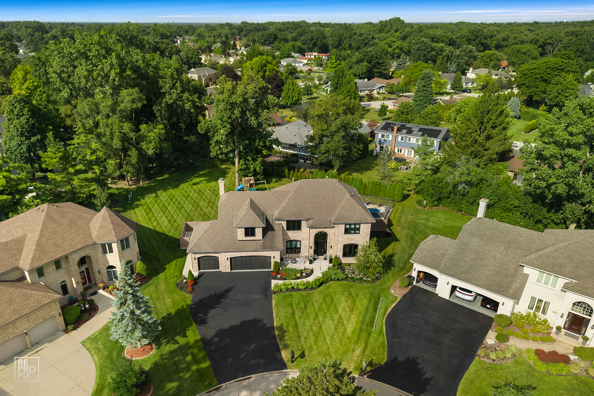 Aerial view of a wooded neighborhood with a brick home and driveway in the foreground — drone photography