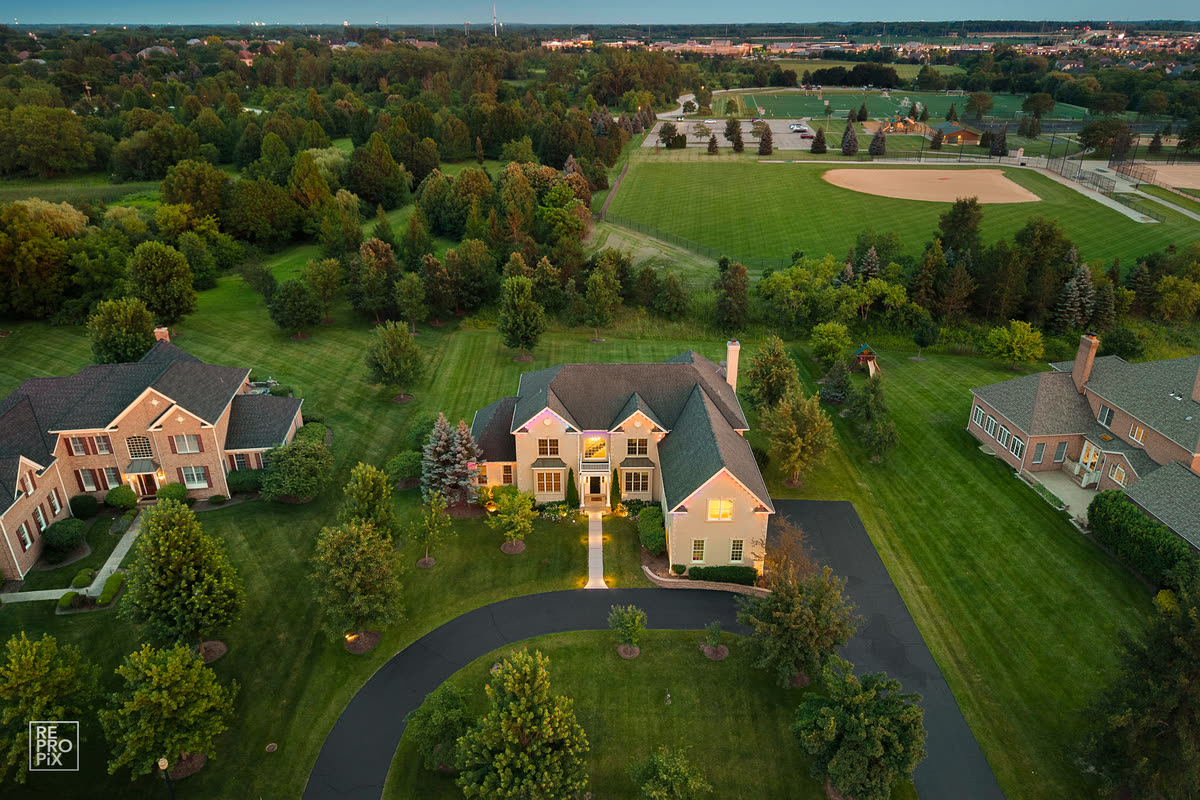 Aerial view of a home on a large lot beside a park with a baseball diamond and a pond — drone photography