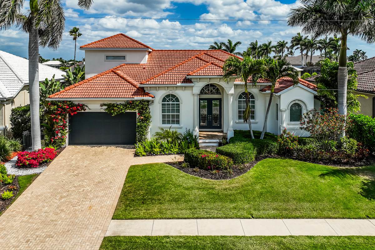 Spanish-tile single-family home with a paved driveway, palms and flowering beds