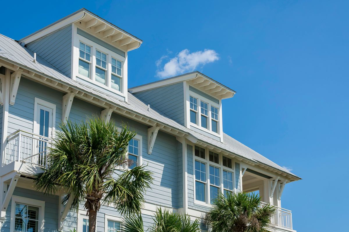 Blue coastal-style home with white trim and a balcony against a clear sky