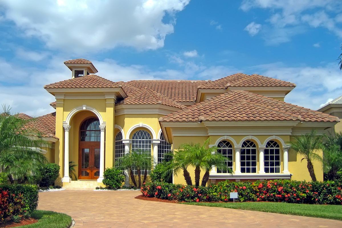 Mediterranean-style home with arched windows, a tile roof and flowering landscaping