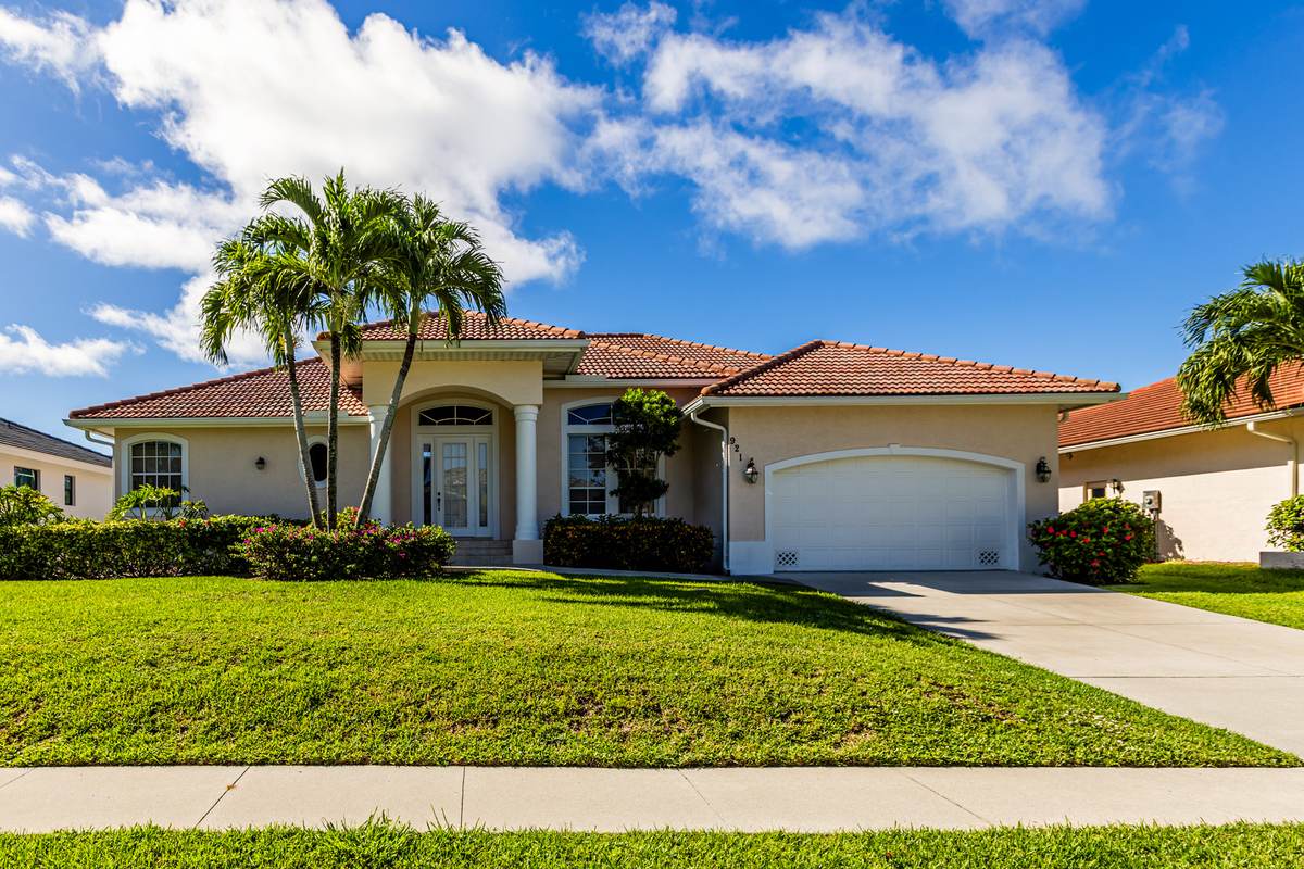 Single-storey home with a tile roof, palms and a clipped lawn under a blue sky