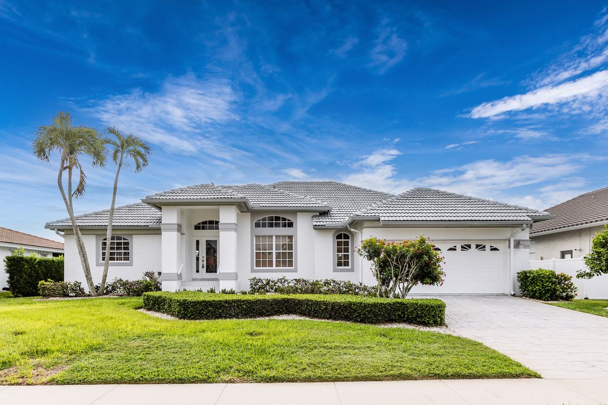 Wide single-storey home with a tile roof, palms and a lawn under an open sky