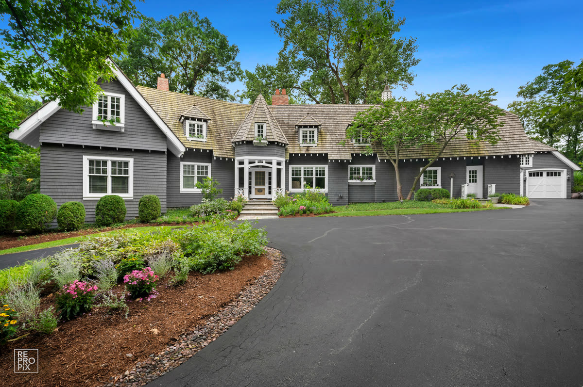 Charcoal shingled Chicago-area home with dormer windows and a curved driveway past flower beds — home exterior photo