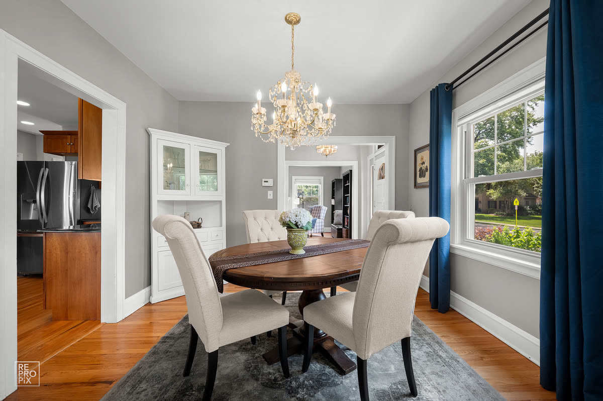 Dining room with a crystal chandelier, oval table and cream upholstered chairs, open through to the kitchen — listing photo