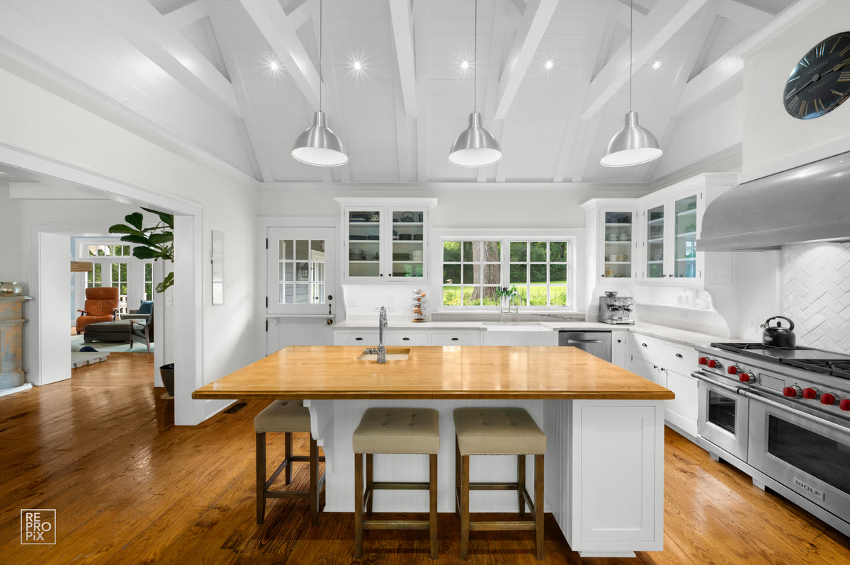 Kitchen under a vaulted beamed ceiling with three pendant lights above a butcher-block island — home interior photography