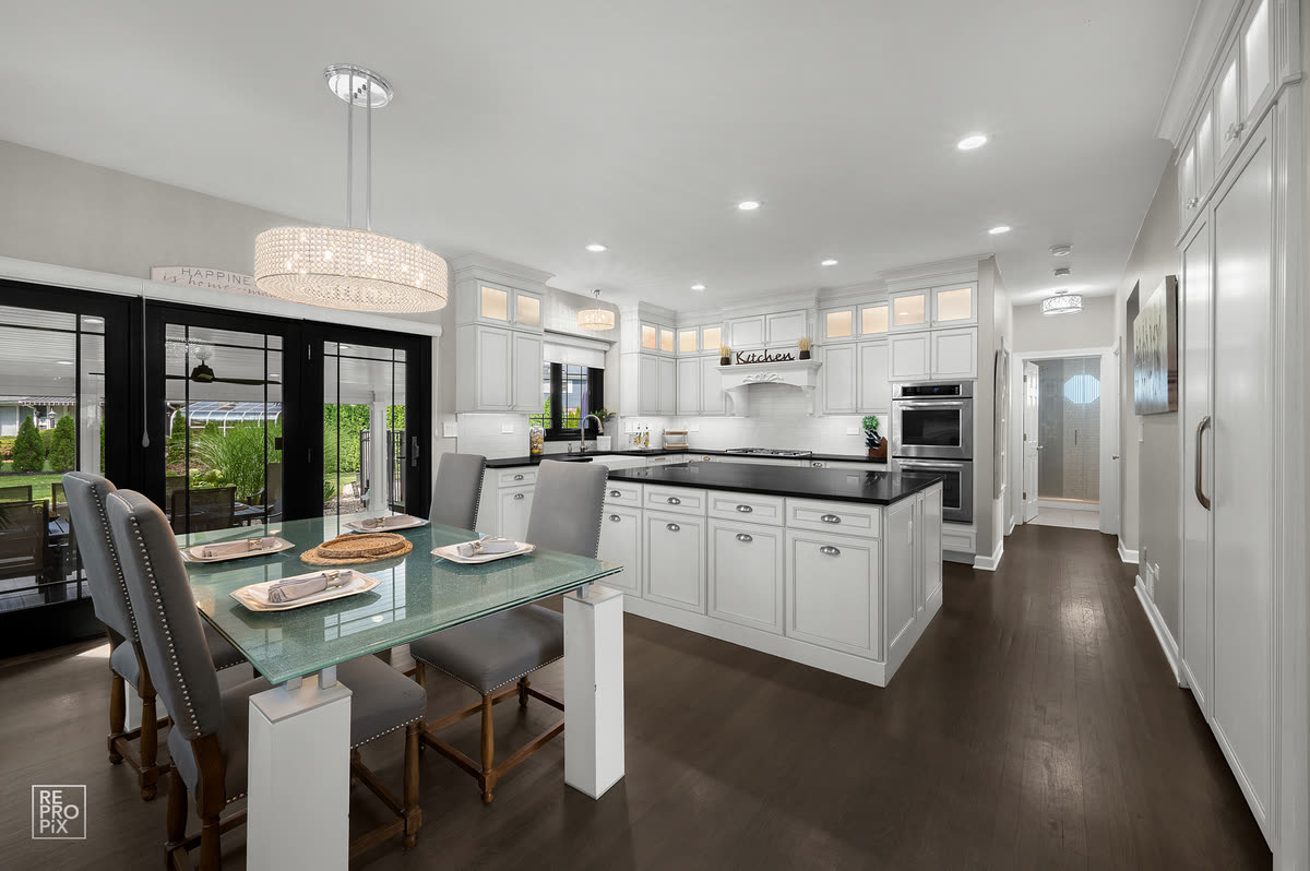 Kitchen and dining space with a glass table, drum chandelier, black counters and dark floors — listing photo