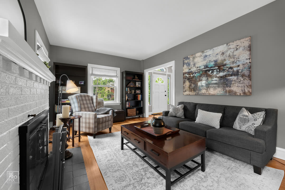 Living room with a white painted brick fireplace, gray sofa and plaid armchair — real estate photography