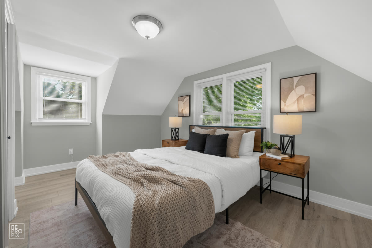 Bedroom under a sloped dormer ceiling with bedside lamps and framed prints — MLS gallery photo