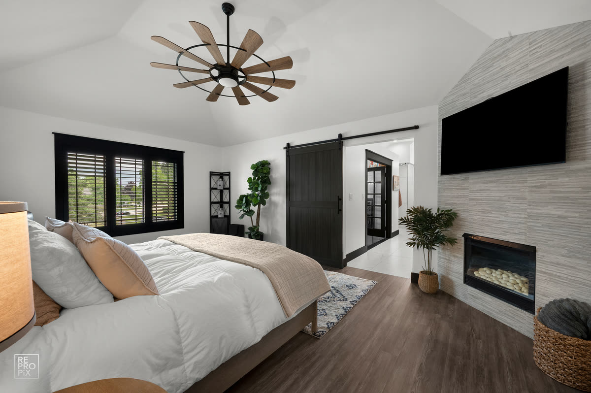 Primary bedroom with a vaulted ceiling, black barn door and a linear fireplace below the television — listing photo