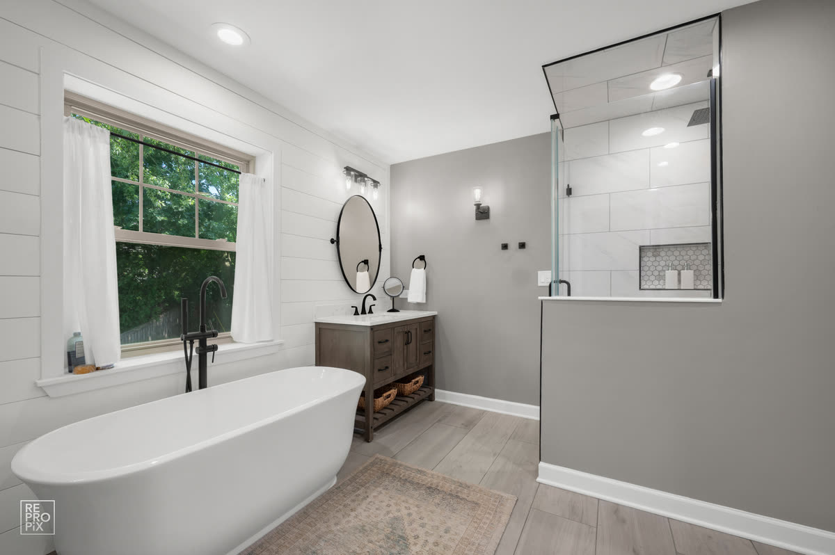 Bathroom with a freestanding tub beneath the window, shiplap walls and a tiled walk-in shower — property photo