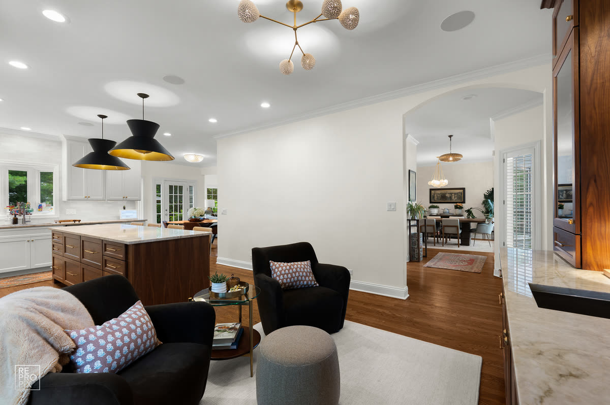 Open living and kitchen space with black and gold pendants and an arched opening to the dining room — listing photo