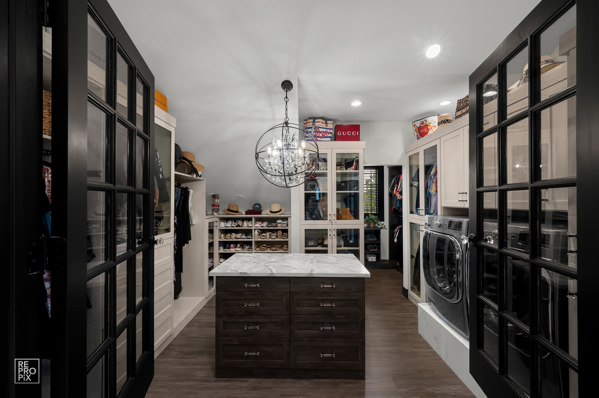 Walk-in dressing room and laundry behind black-framed glass doors, with a marble-topped island — home interior photography