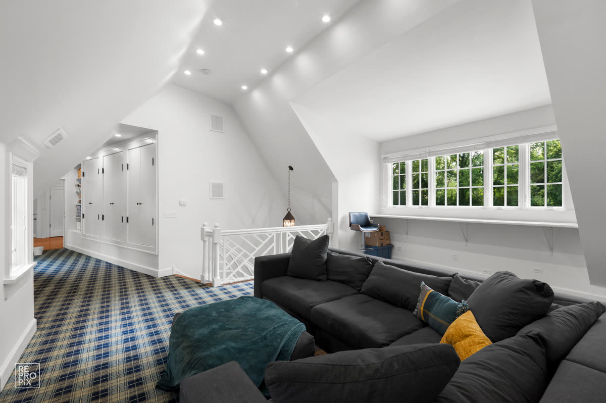 Attic lounge with plaid carpet, a gray sectional and dormer windows — MLS gallery photo