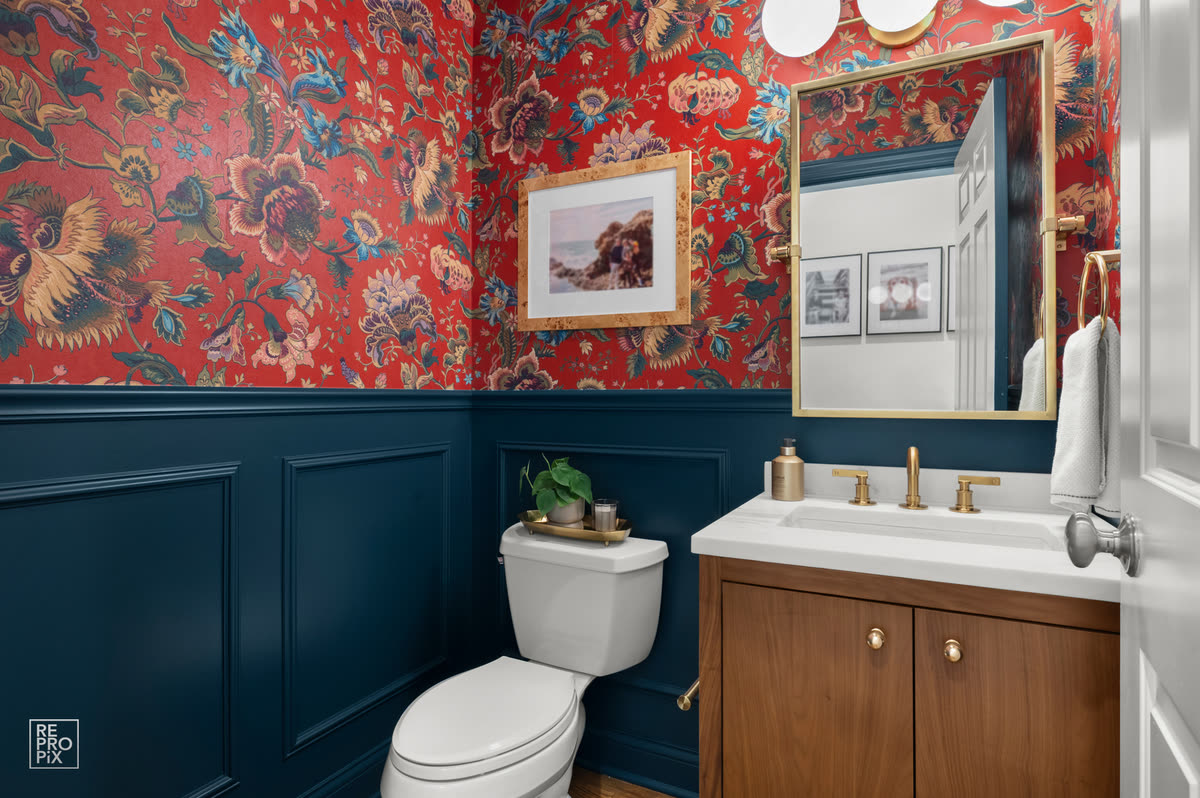 Powder room with bold red floral wallpaper above navy wainscoting and a wood vanity — property photo