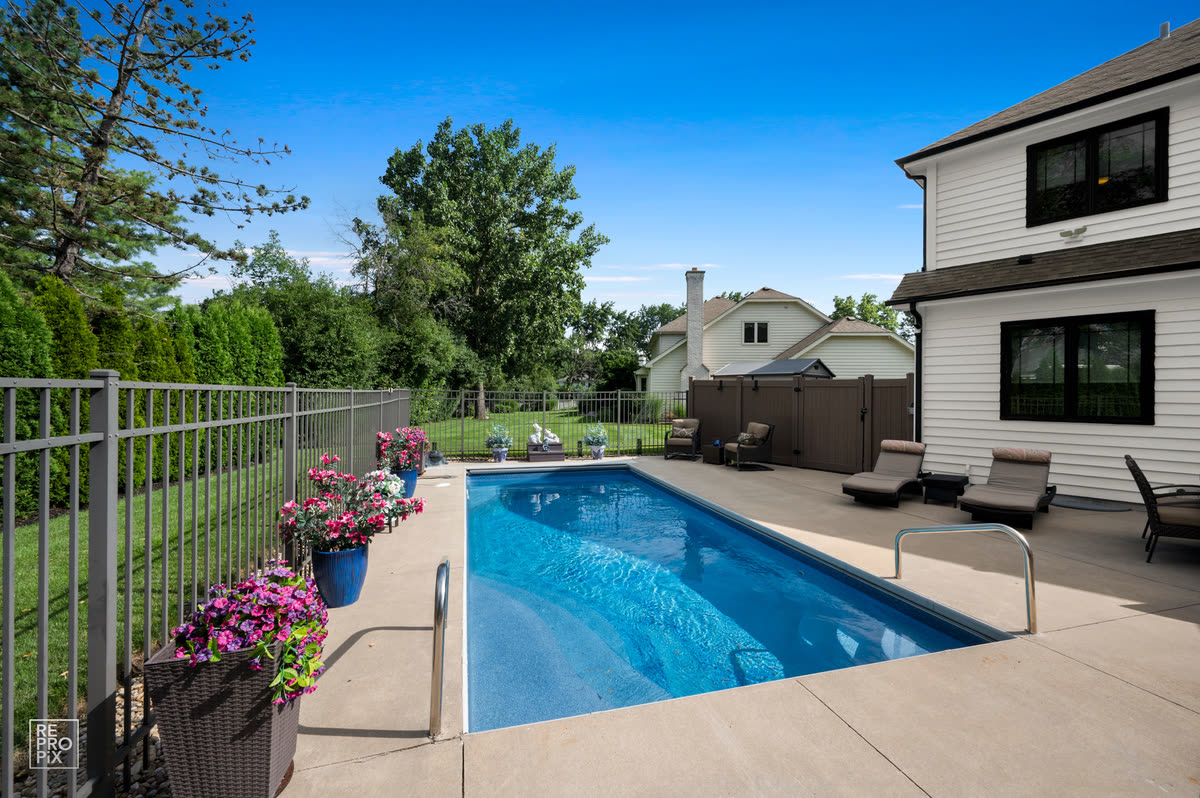 Fenced backyard pool beside a white clapboard house, with planted flowers along the deck — property photo