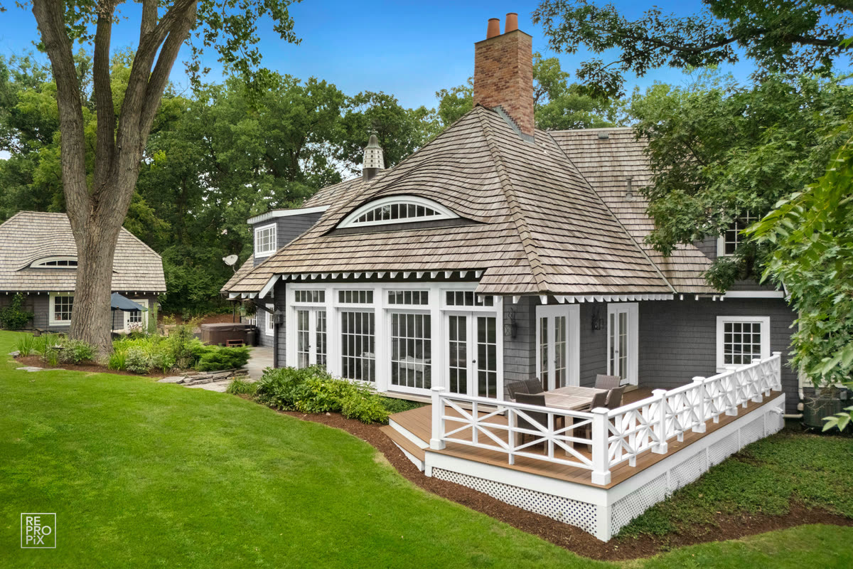 Rear elevation of a shingled home with a conical turret roof, white deck railing and brick chimney — home exterior photo